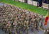 Soldiers in camouflage uniforms march in formation on a street