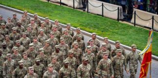 Soldiers in camouflage uniforms march in formation on a street