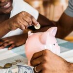 Child placing coin into pink piggy bank