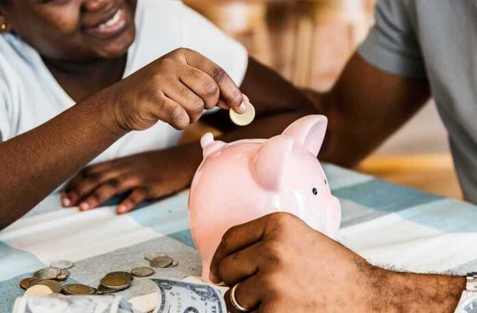 shutterstock_796176295 Child placing coin into pink piggy bank